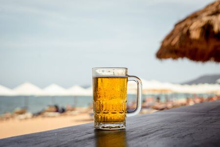 Mug of cold beer with foam on the table. Against the background of the sea. The Restaurantの写真素材