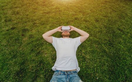 A young man plays a game in glasses of virtual reality lying on the grass.の写真素材