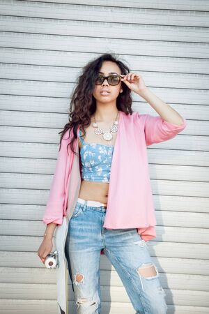 Young girl with skateboard on the background of the big gray wall.の写真素材