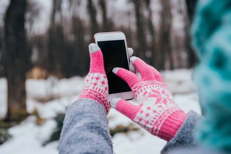 Woman using smartphone in winter with gloves for touch screens. Backgoundの写真素材