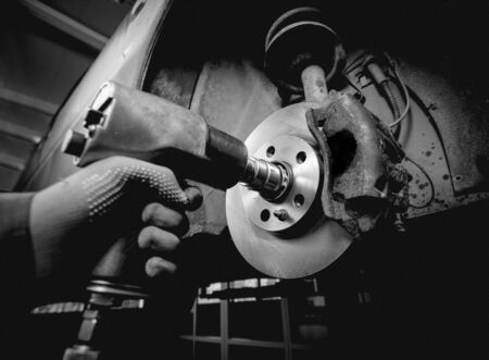 Professional car mechanic working with pneumatic wrench in auto repair service. Repair of wheelsの写真素材