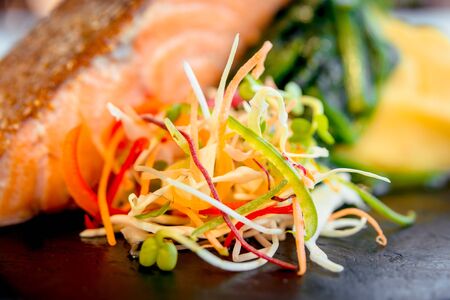 Fish with vegetables on a black plate.の写真素材