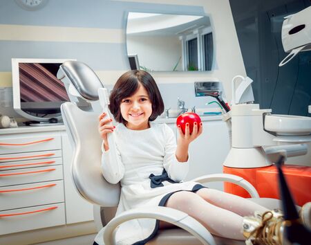 Little girl smiling, holding in hands a toothbrush and an apple.の写真素材