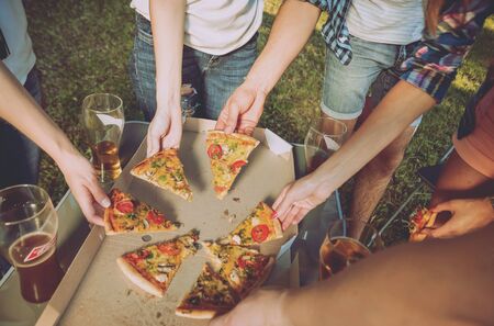 Cheerful friends on picnic in the park. Eating pizza.の写真素材