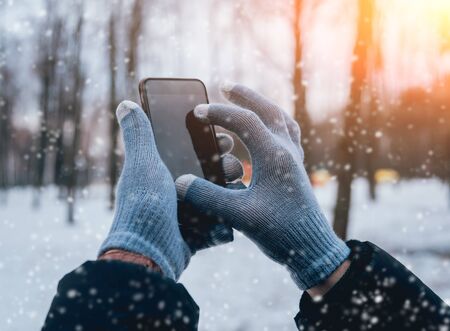 Man using smartphone in winter with gloves for touch screens. Backgoundの写真素材