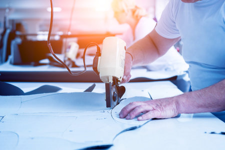 Male worker uses electric cutting fabric machine. Fabric industry production line. Textile factory....