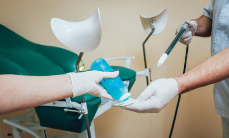 Proctologist holding an anoscope against a proctological chair.