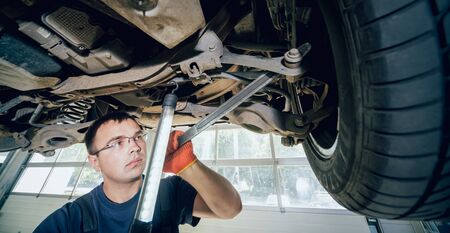 Car mechanic examining car suspension of lifted automobileの写真素材