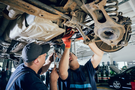 Car mechanics repair car suspension of lifted automobile at repair service station. Background