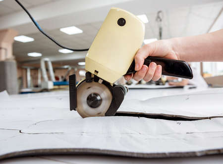 Female worker uses electric cutting fabric machine. Fabric industry production line. Textile factory. Working tailoring process cloth. Modern equipmentの写真素材