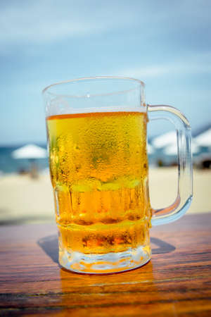 Mug of cold beer with foam on the table. Against the background of the sea. The Restaurantの写真素材