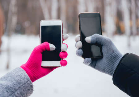 Couple using smartphone in winter with gloves for touch screens. Backgoundの写真素材