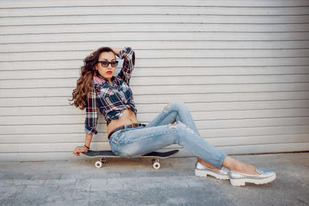 Young girl with skateboard on the background of the big gray wall.の写真素材