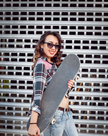 Young girl with skateboard on the background of the big gray wall.の写真素材