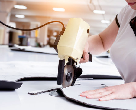 Female worker uses electric cutting fabric machine. Fabric industry production line. Textile...