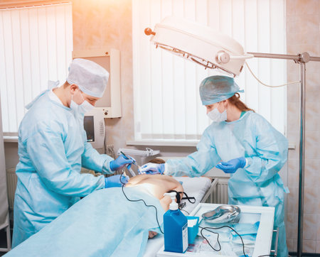 Surgeon and assistant in operating room with surgery equipment.