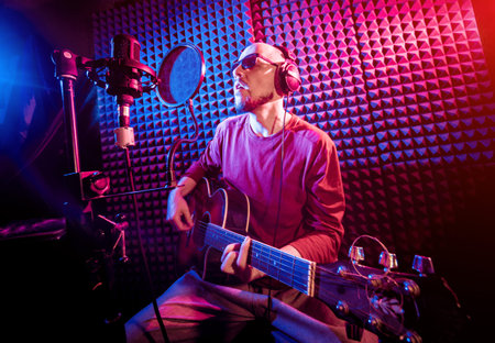 The singer sings with a microphone and playing guitar in the recording studio.