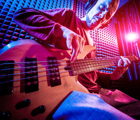 Young man playing on the bass guitar in sound recording studio.