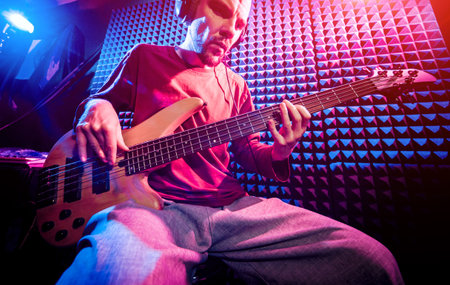 Young man playing on the bass guitar in sound recording studio.