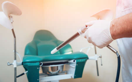 Proctologist holding an anoscope against a proctological chair.の写真素材