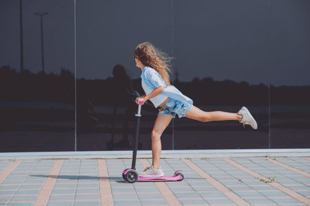 Little girl riding scooter outdoors. Street urban background.