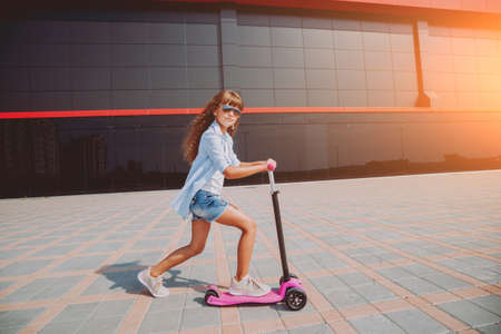 Little girl riding scooter outdoors. Street urban background.の写真素材