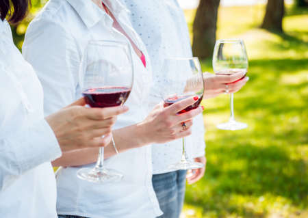 Young beautiful girls with glass of red wine in the parkの写真素材
