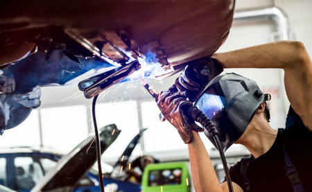 Car mechanic with protective mask welding car. Service station