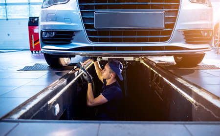 Car mechanic examining car suspension of lifted automobile at service stationの写真素材