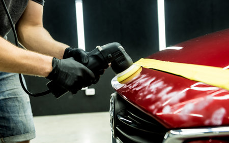 Car service worker polishes a car details with orbital polisher.