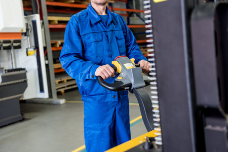 A worker in a warehouse uses a hand pallet stacker to transport pallets.