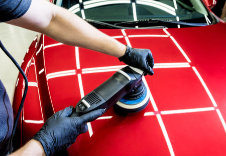 Car service worker polishes a car details with orbital polisher.