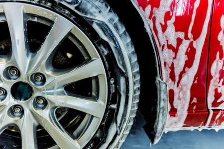 Washing red car with active foam at car wash service.の写真素材