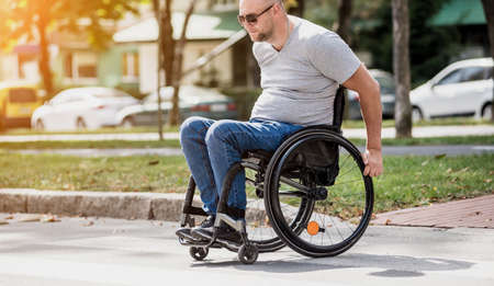 Handicapped man in wheelchair crossing street roadの写真素材