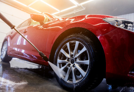 Worker washing car with high pressure water at a car wash.の写真素材