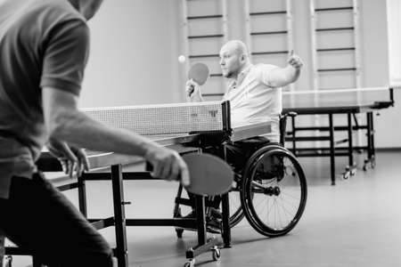 Adult disabled man in a wheelchair play at table tennis with his coachの写真素材