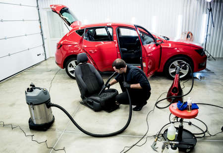 Car service worker cleaning car seat with vacuum cleaner.の写真素材