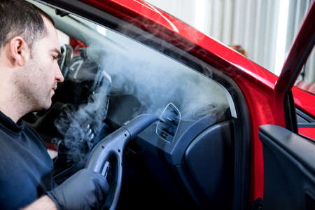 Car service worker cleans interiror with steam cleanerの写真素材