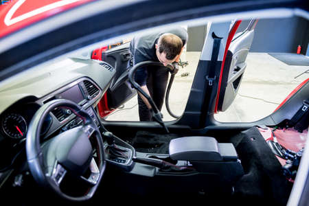 Car service worker cleaning car interior with a vacuum cleanerの写真素材