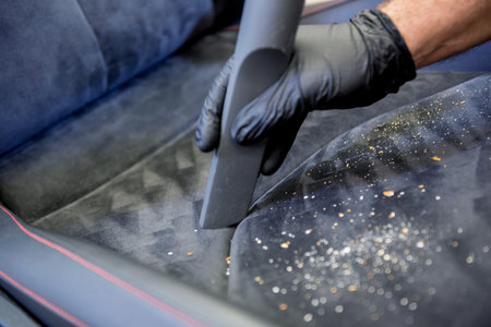 Car service worker cleaning car seat with vacuum cleaner.