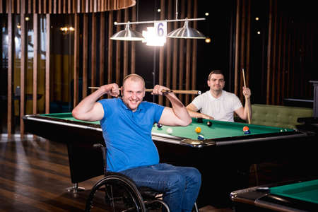 Adult men with disabilities in a wheelchair play billiards in the clubの写真素材