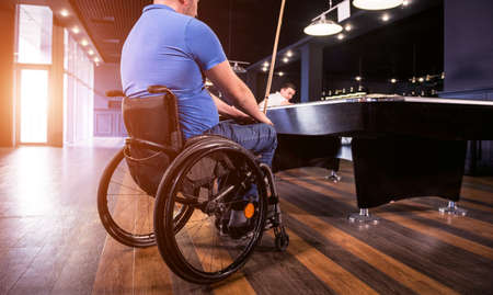 Adult men with disabilities in a wheelchair play billiards in the clubの写真素材