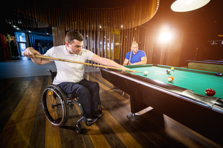 Adult men with disabilities in a wheelchair play billiards in the club