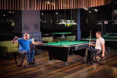 Adult men with disabilities in a wheelchair play billiards in the club