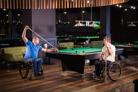 Adult men with disabilities in a wheelchair play billiards in the club