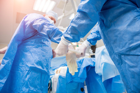 Assistant helps the surgeon put on latex gloves and surgical gown before the operation.