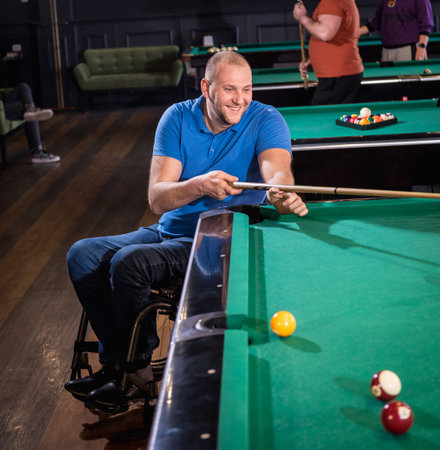 Adult man with disability in a wheelchair play billiards in the club