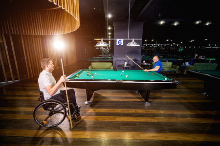 Adult men with disabilities in a wheelchair play billiards in the club