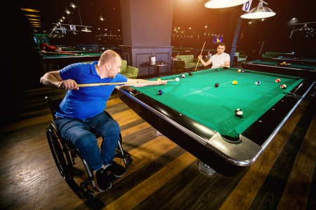 Adult men with disabilities in a wheelchair play billiards in the club