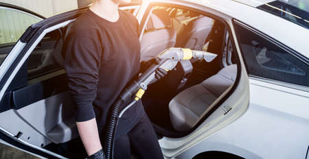 Worker cleans car interior with vacuum cleanerの写真素材